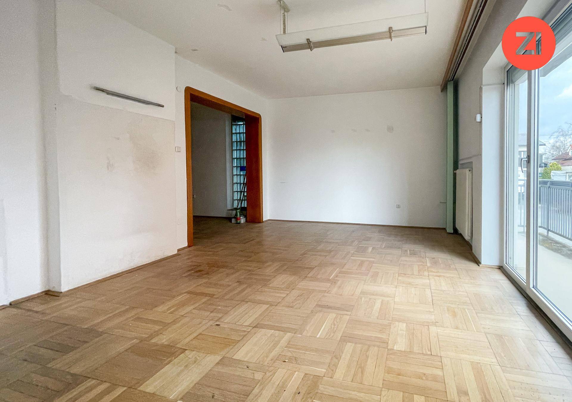 Geräumiger Raum mit Parkettboden und breiter Fensterfront, die viel Tageslicht hereinlässt.