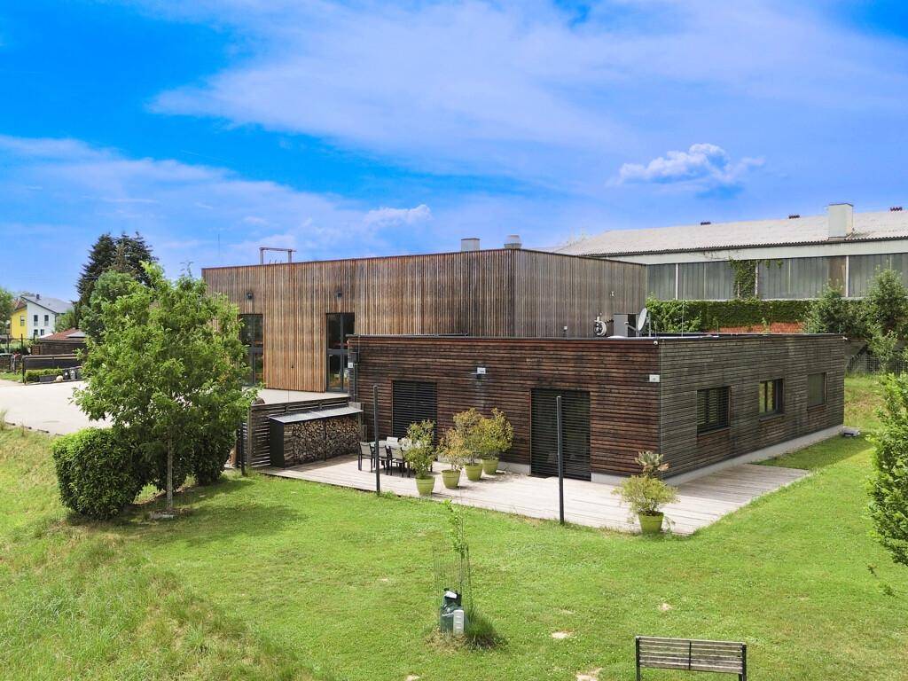 Moderne Holzfassade des Gebäudes mit einer einladenden Holzterrasse, Gartenmöbeln und grüner Rasenfläche.