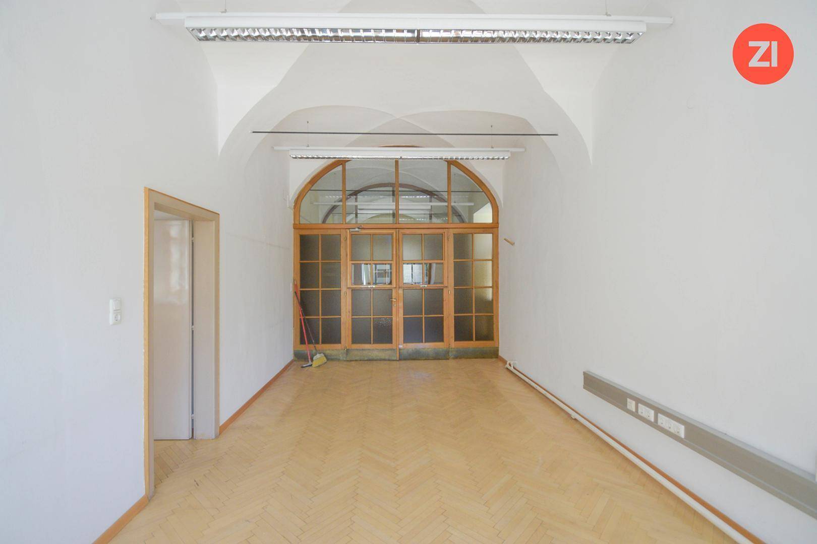 Großer Raum mit gewölbter Decke, Holztüren und großen Fenstern, ideal für Versammlungen oder Großraumbüros.