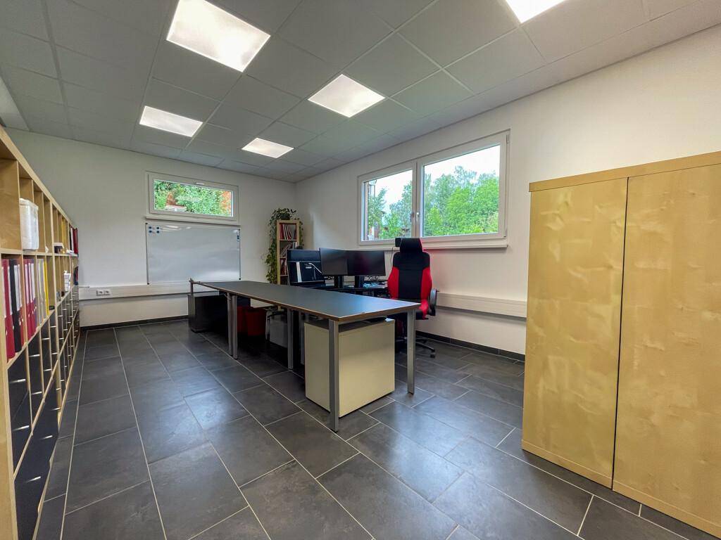 Geräumiges Büro mit dunklem Fliesenboden, mehreren Arbeitsplätzen und großen Fenstern für viel Licht.