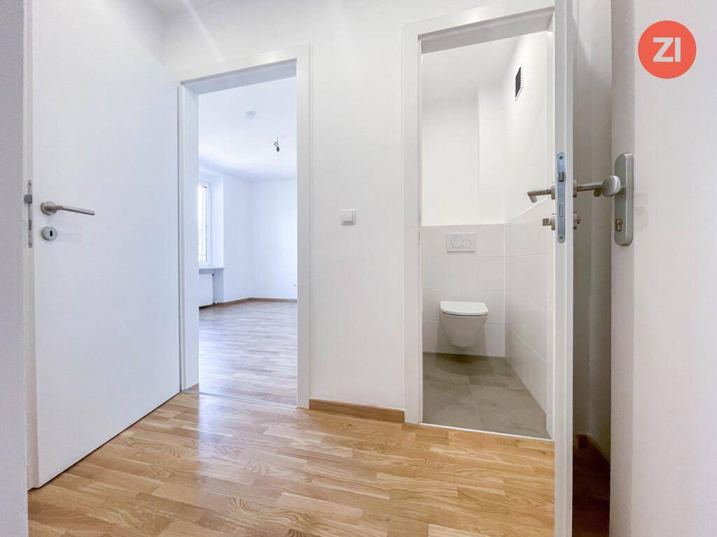Heller Flur mit Parkettboden, der zu einem weiteren Raum und einer separaten Toilette führt.