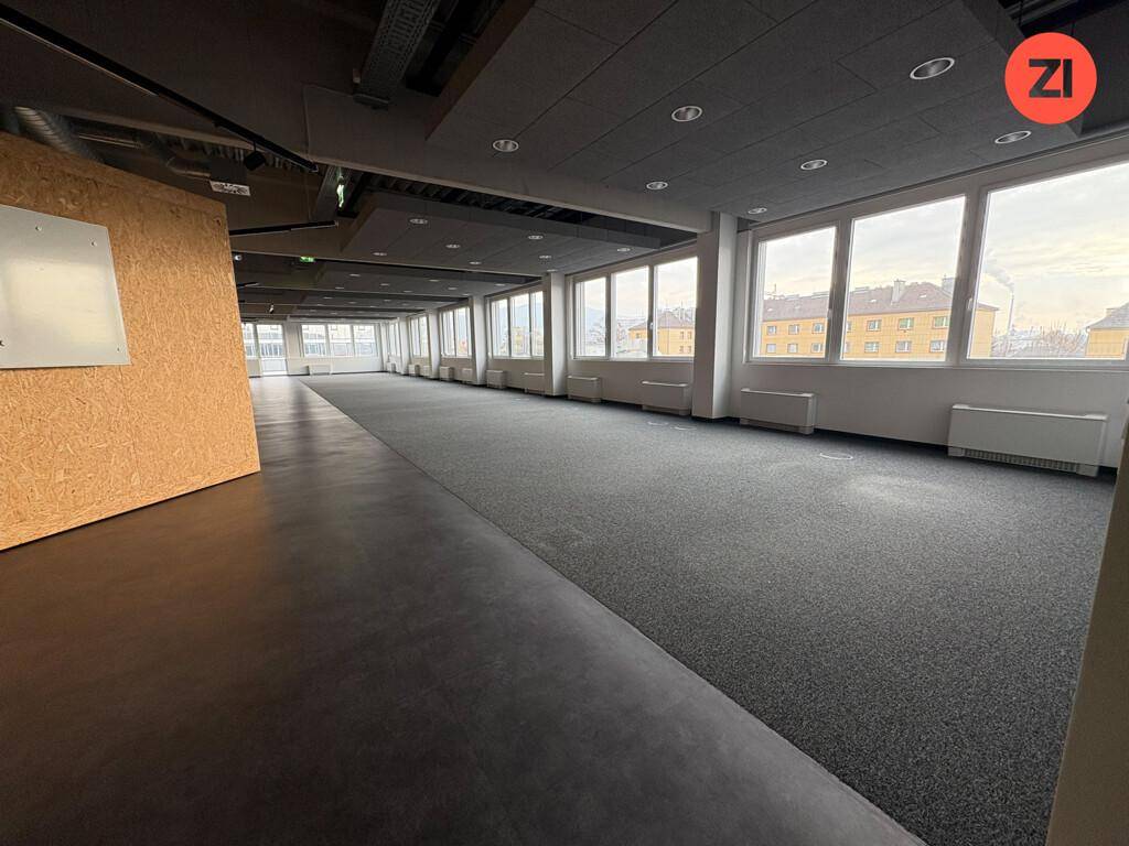 Geräumiger, offener Bürobereich mit Teppichboden, großen Fenstern und Blick auf die Stadt.