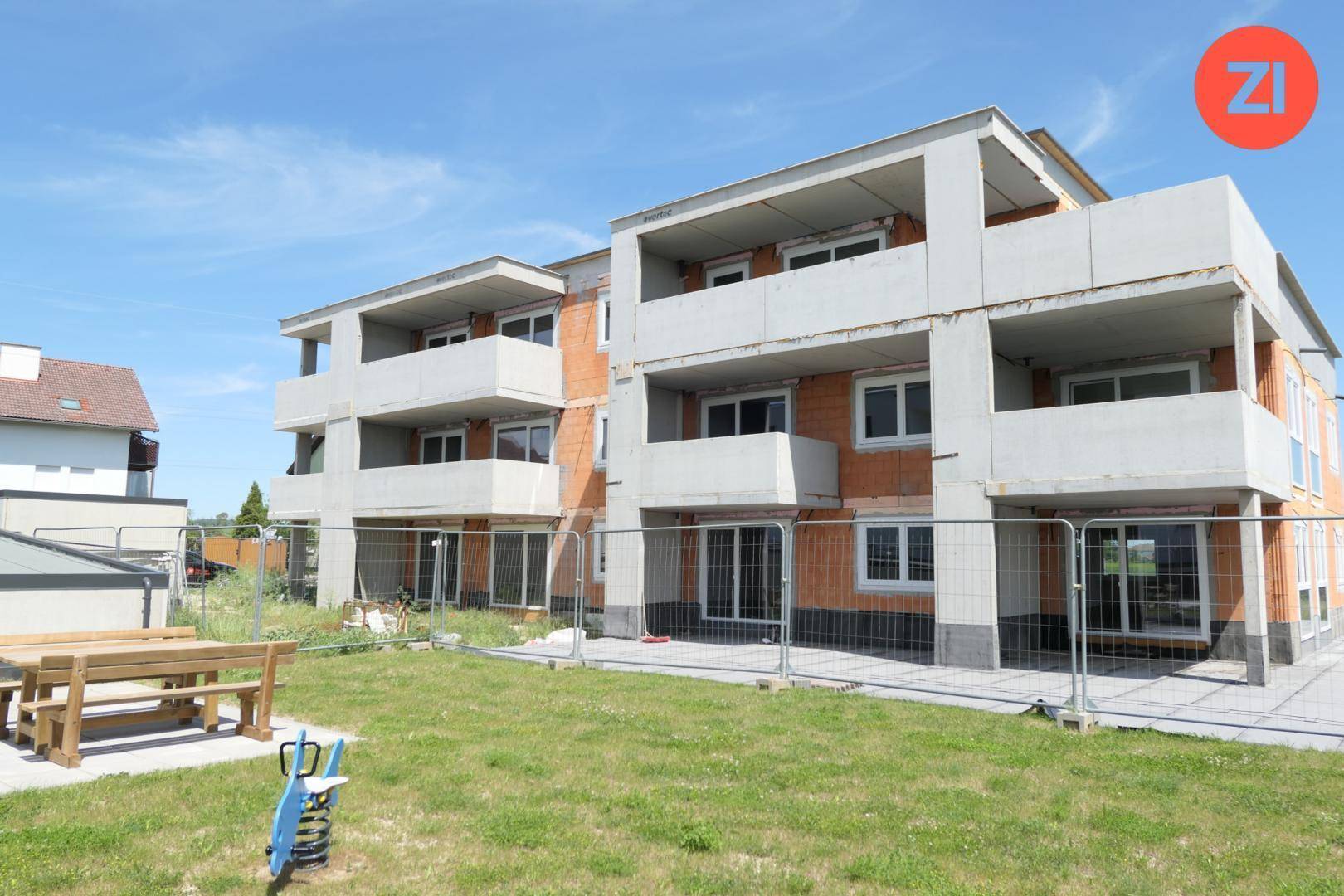 Neubau-Mehrfamilienhaus mit Balkonen und einer Grünfläche im Vordergrund, noch im Bau.