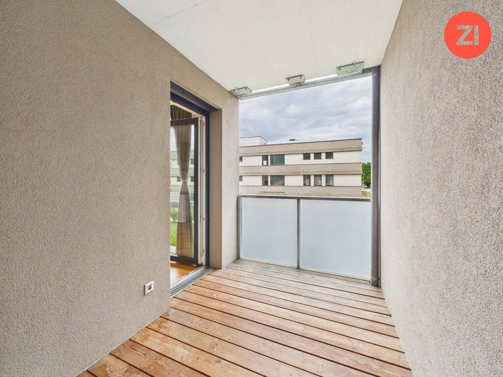 Balkon mit Holzboden und Glasbrüstung, bietet einen Blick auf die umliegenden Gebäude.