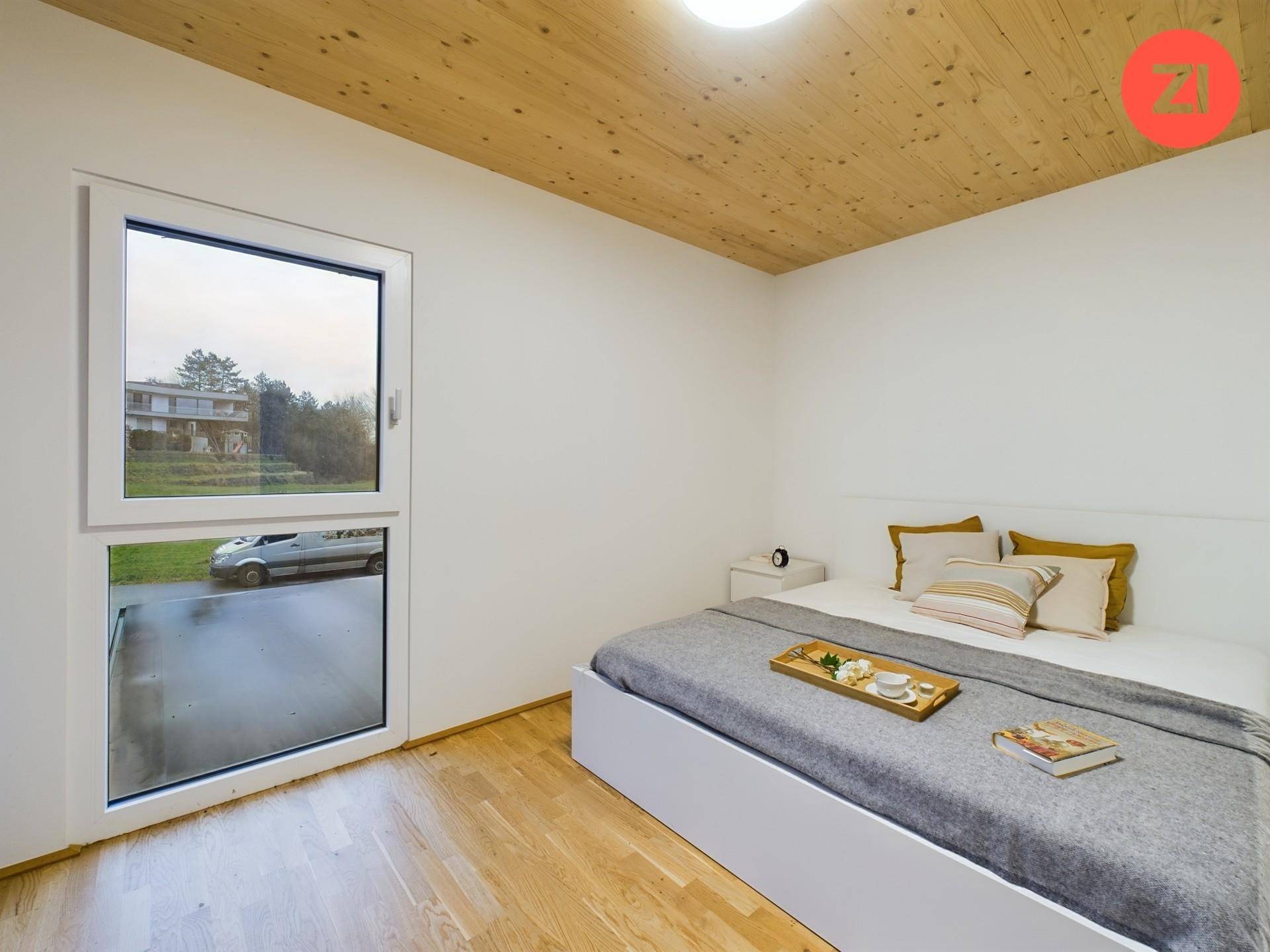 Helles Schlafzimmer mit Holzboden, großem Fenster und Blick ins Grüne.