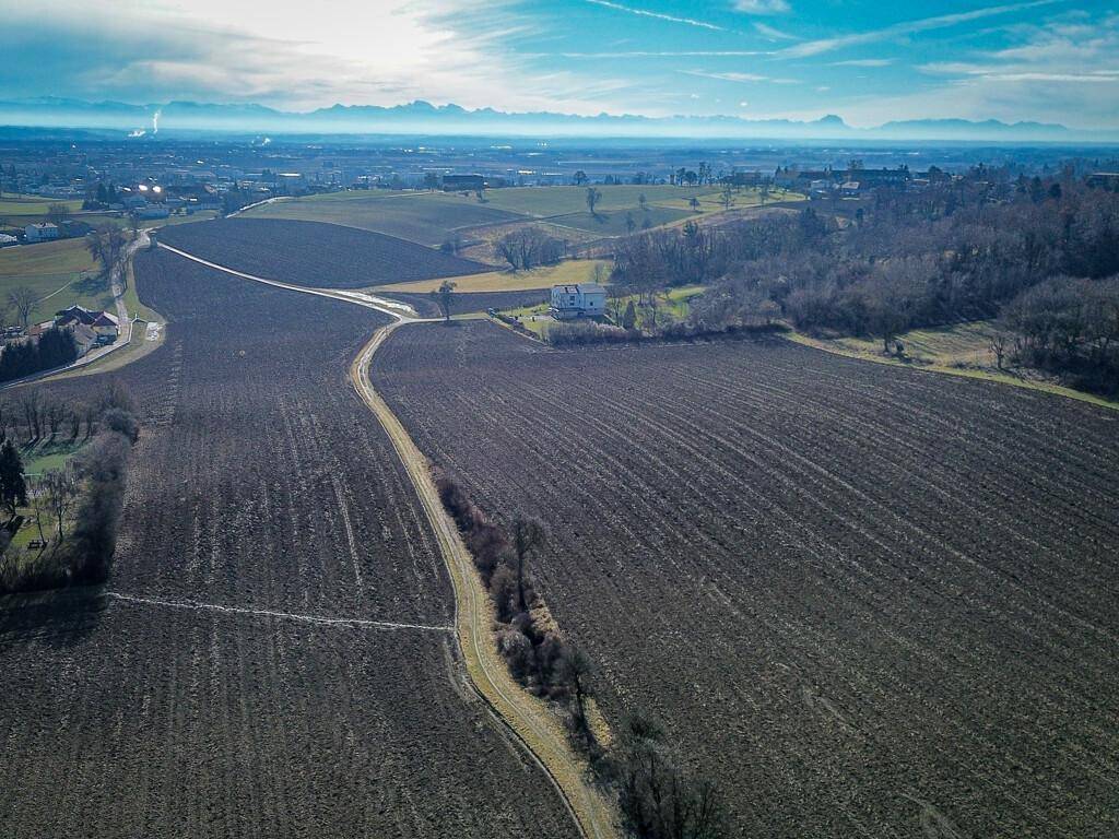 Weitläufige Ackerflächen mit Wegen und einem einzelnen Gebäude, umgeben von einer weiten Landschaft.