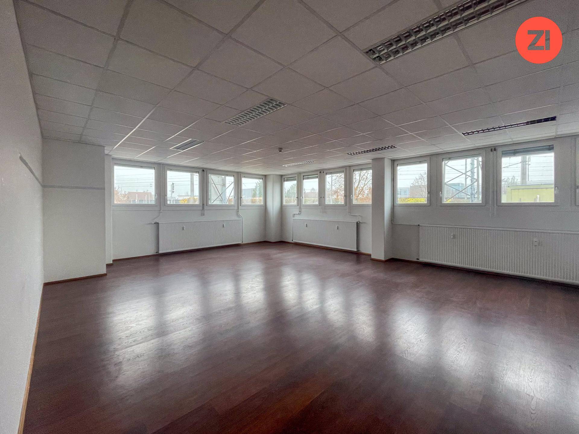 Geräumiges Büro mit Holzoptik-Boden, vielen Fenstern und einer abgehängten Decke mit integrierter Beleuchtung.