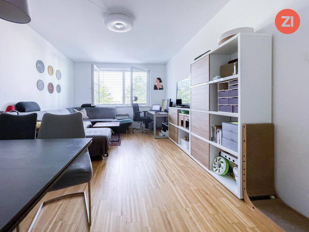 Geräumiges Wohnzimmer mit Holzboden, Sofa und Arbeitsbereich am Fenster.