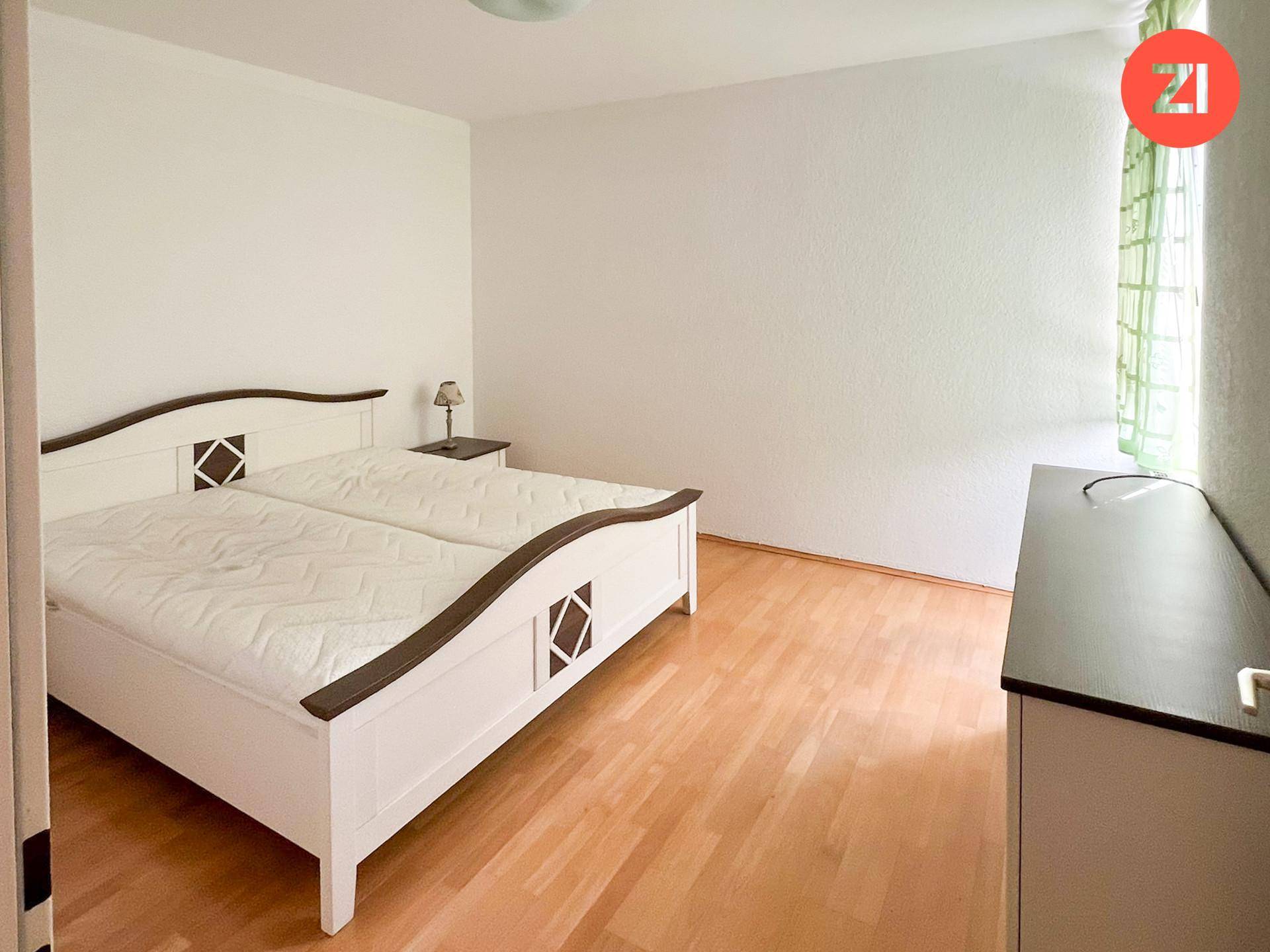 Helles Schlafzimmer mit einem traditionellen weißen Doppelbett und warmem Holzfußboden.