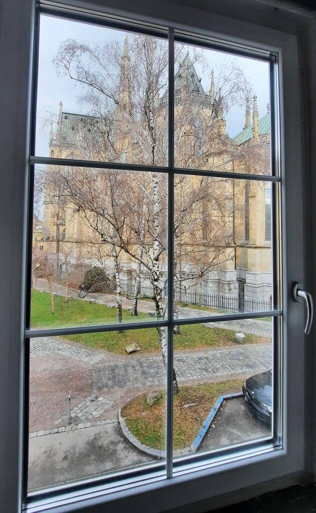 Blick aus einem Fenster auf eine beeindruckende historische Kirche und kahle Bäume im Winter.