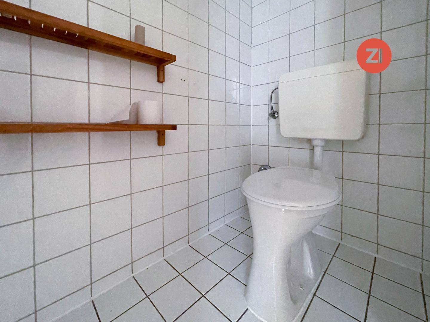 Separates WC mit weißen Fliesen und einfacher, funktionaler Ausstattung, inklusive Holzregalen.