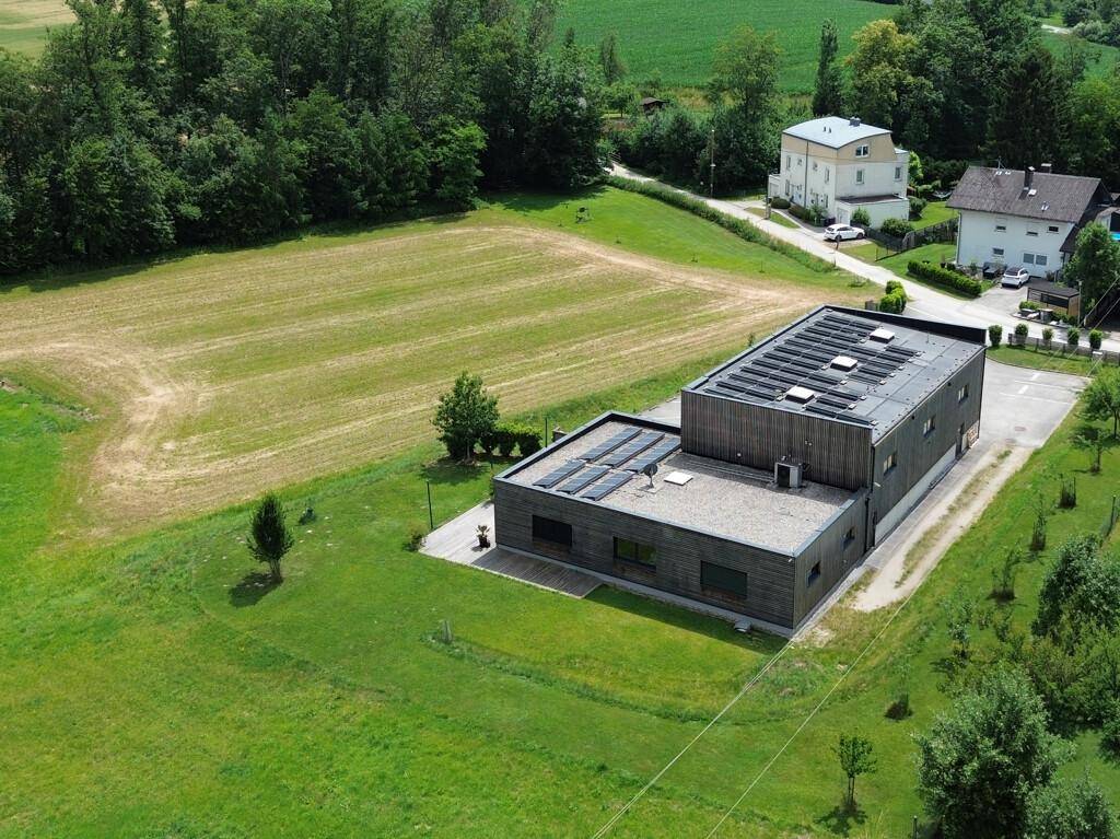 Weitläufige Luftaufnahme des Gebäudes mit Solaranlagen auf dem Dach, umgeben von Feldern und Bäumen.