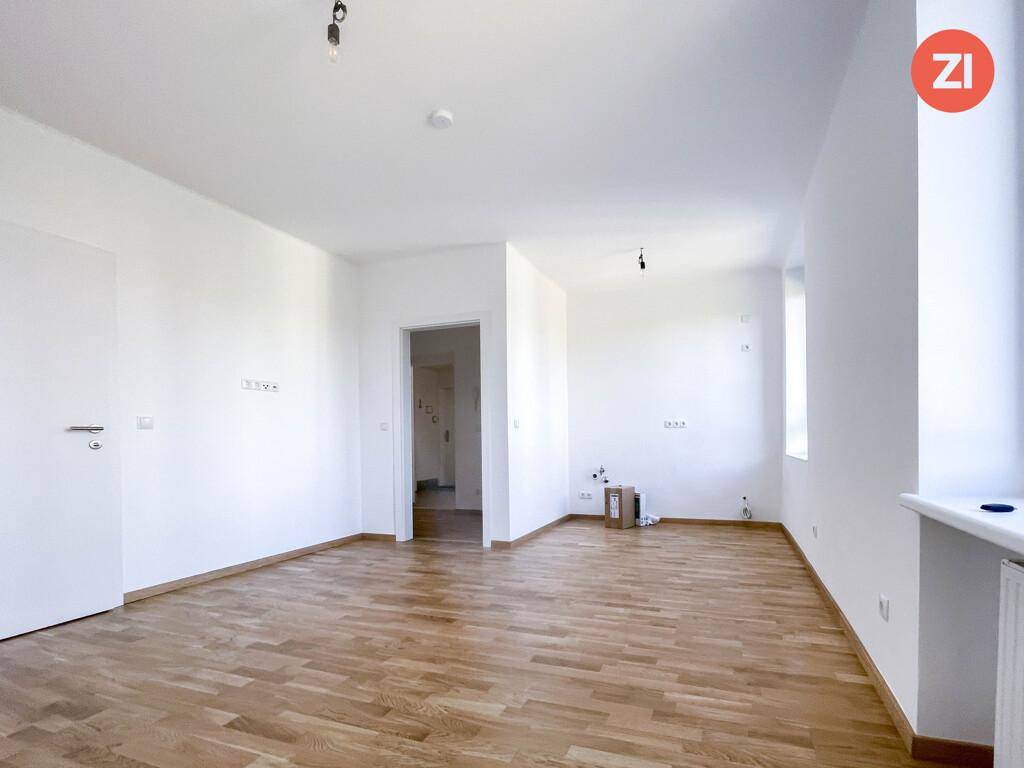Geräumiger, heller Wohnbereich mit Parkettboden, weißen Wänden und einem Fenster.