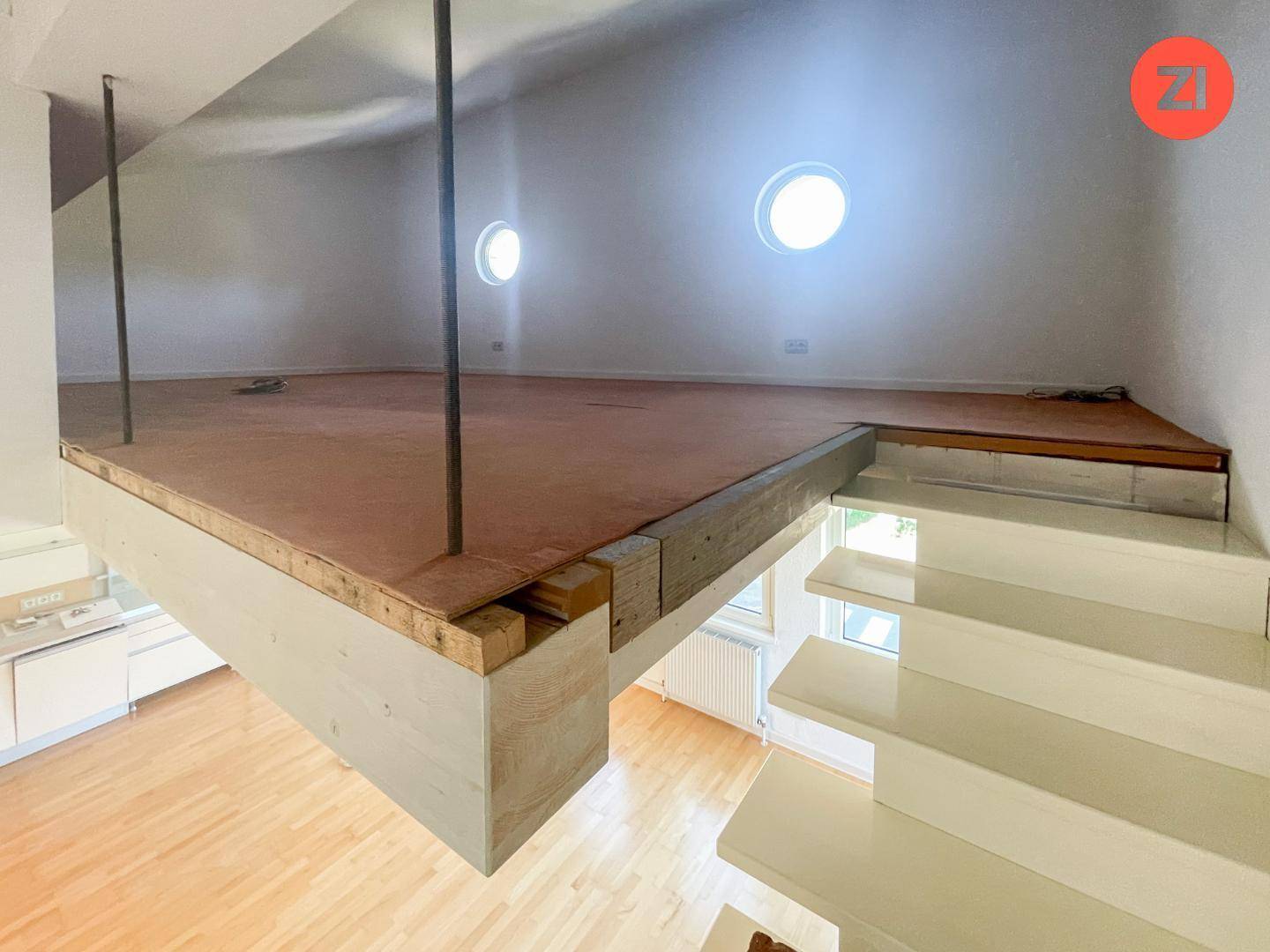 Offene Galerie oder Loftbereich im Bau, zugänglich über eine moderne Treppe, mit runden Fenstern.