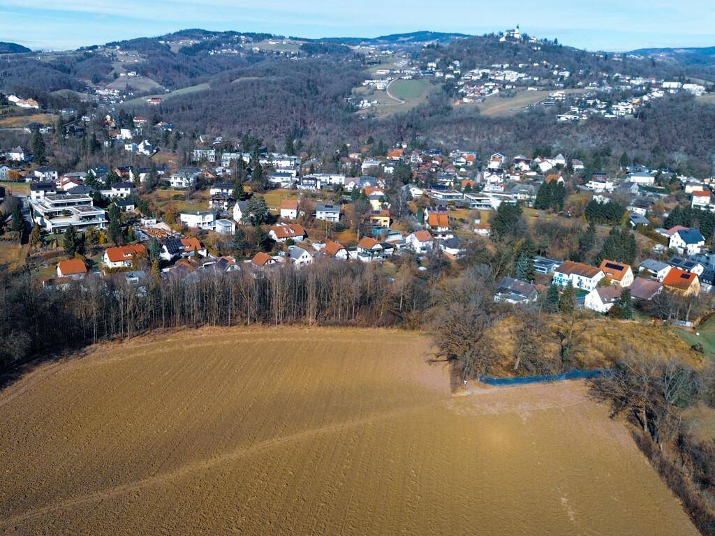 Luftaufnahme eines Feldes mit Blick auf ein dicht besiedeltes Dorf in einer hügeligen Region.