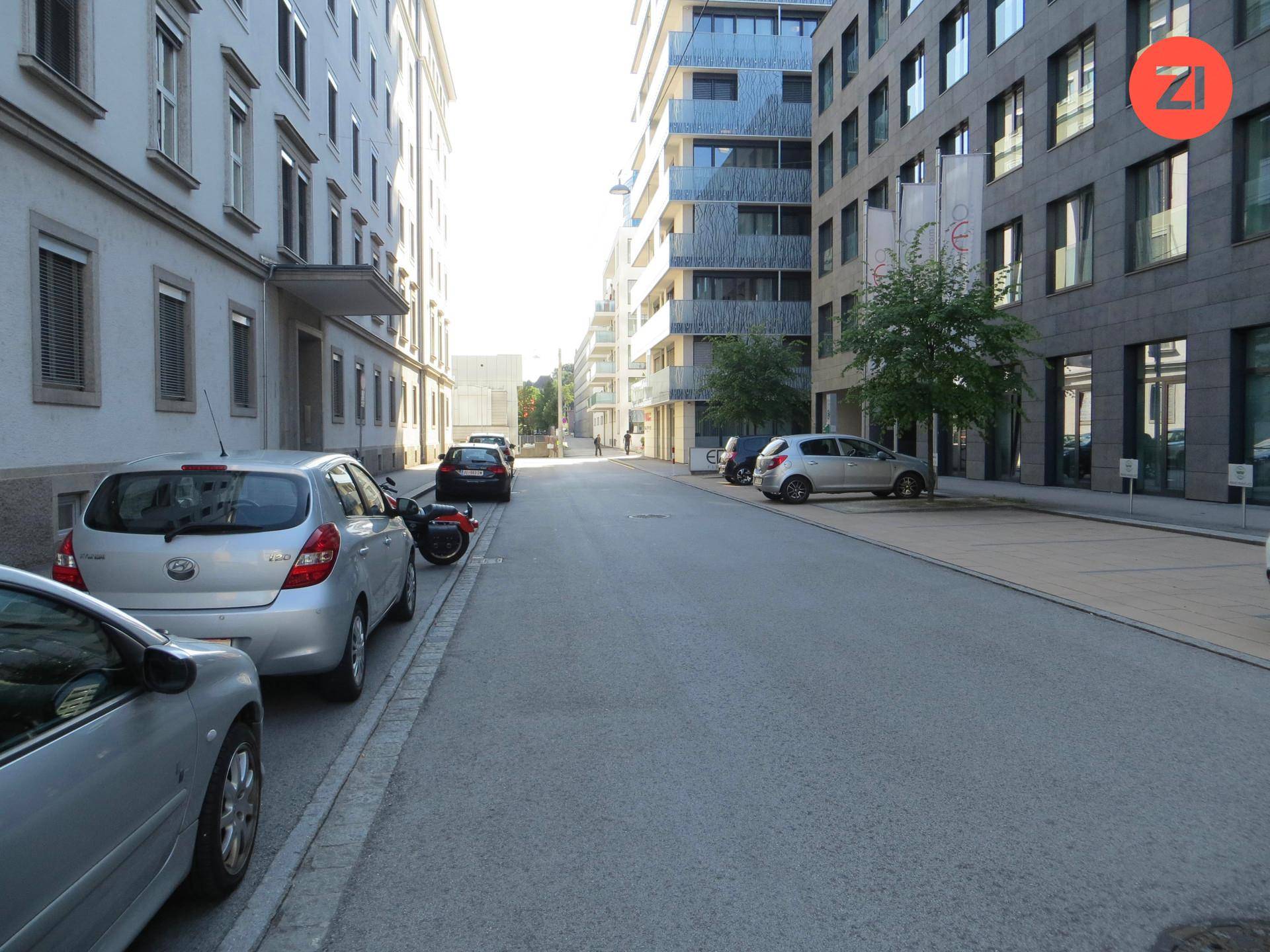 Ruhige Wohnstraße mit modernen Gebäuden und parkenden Autos, umgeben von urbaner Architektur.
