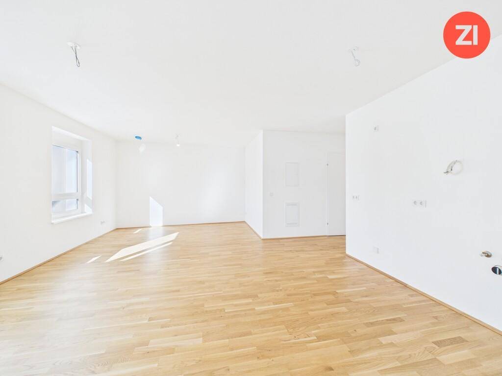 Geräumiges, leeres Wohnzimmer mit hellem Parkettboden und viel natürlichem Licht durch große Fenster.