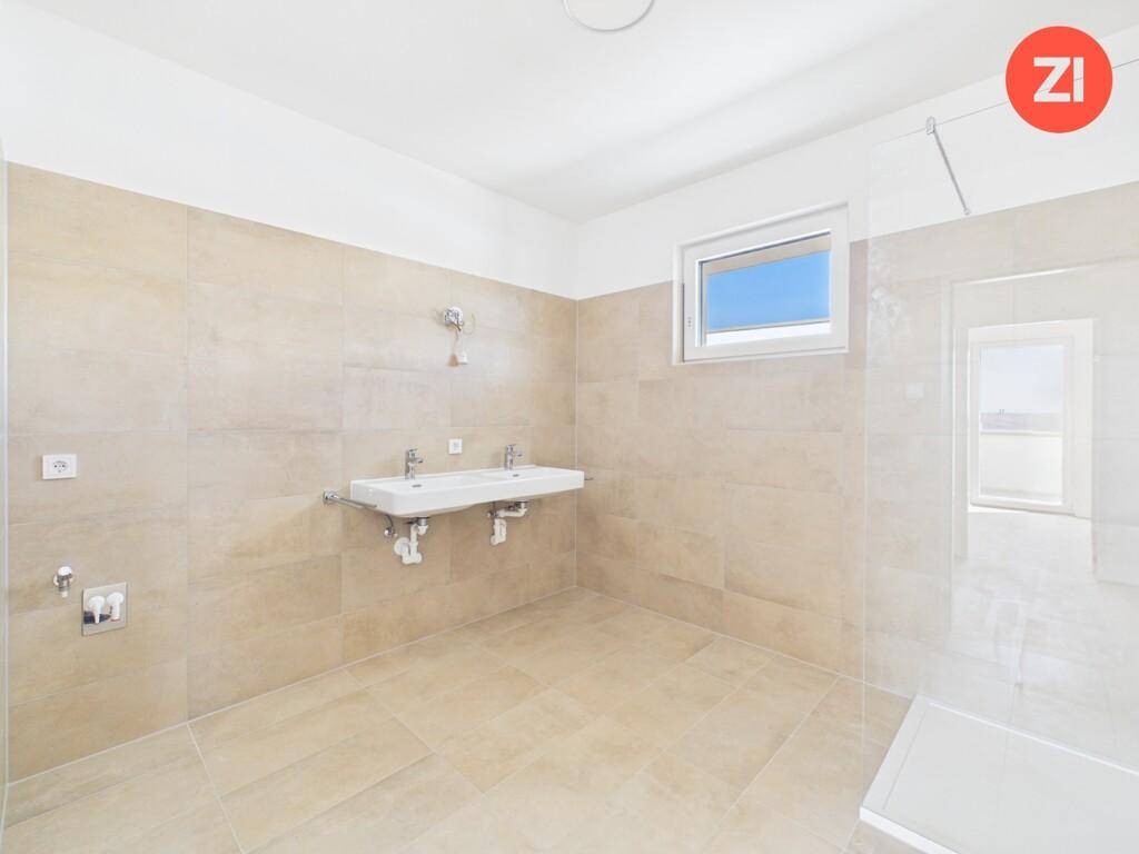 Modernes Badezimmer mit beigefarbenen Fliesen, Doppelwaschbecken und Fenster für natürliches Licht.
