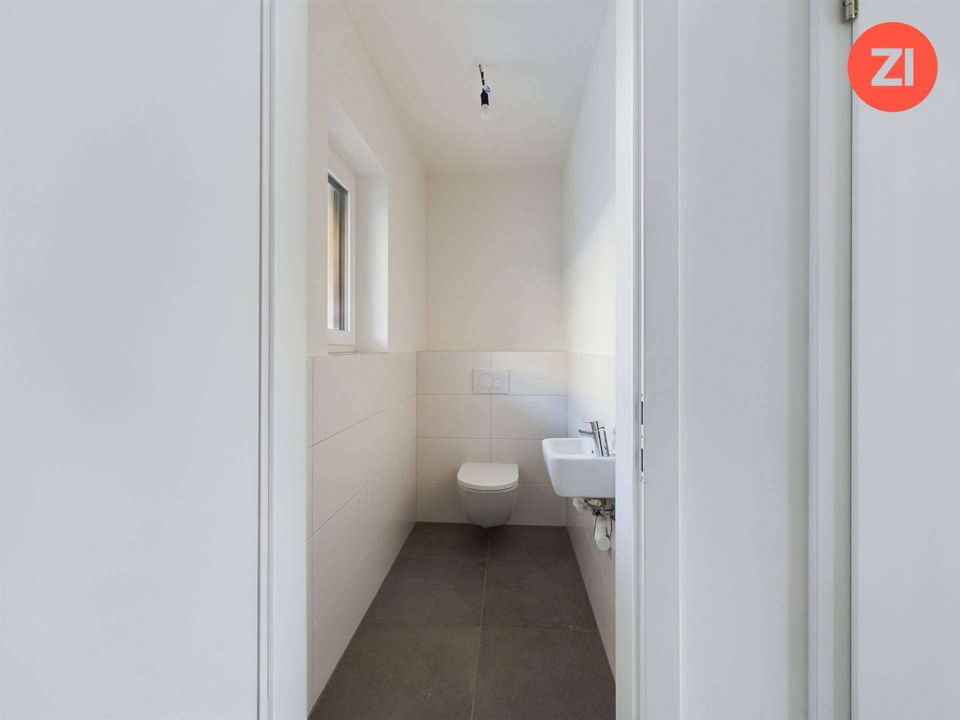 Kleines Gäste-WC mit wandmontierter Toilette, Waschbecken und einem Fenster für natürliche Belüftung.