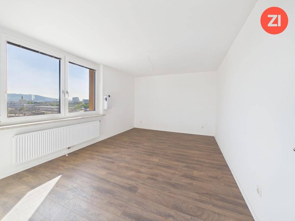 Helles Schlafzimmer mit Holzboden und weitem Blick über die Stadt.