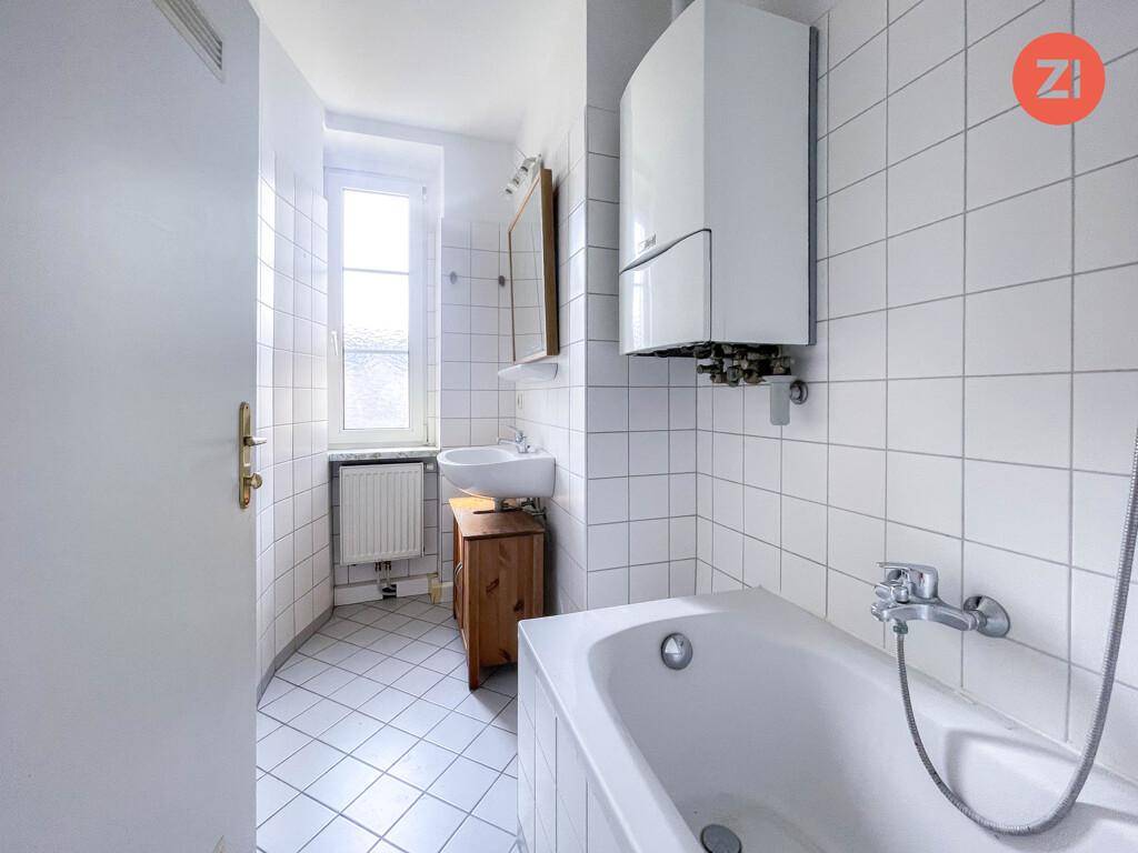 Helles Badezimmer mit Badewanne, Waschbecken auf Holzunterschrank und Fenster.