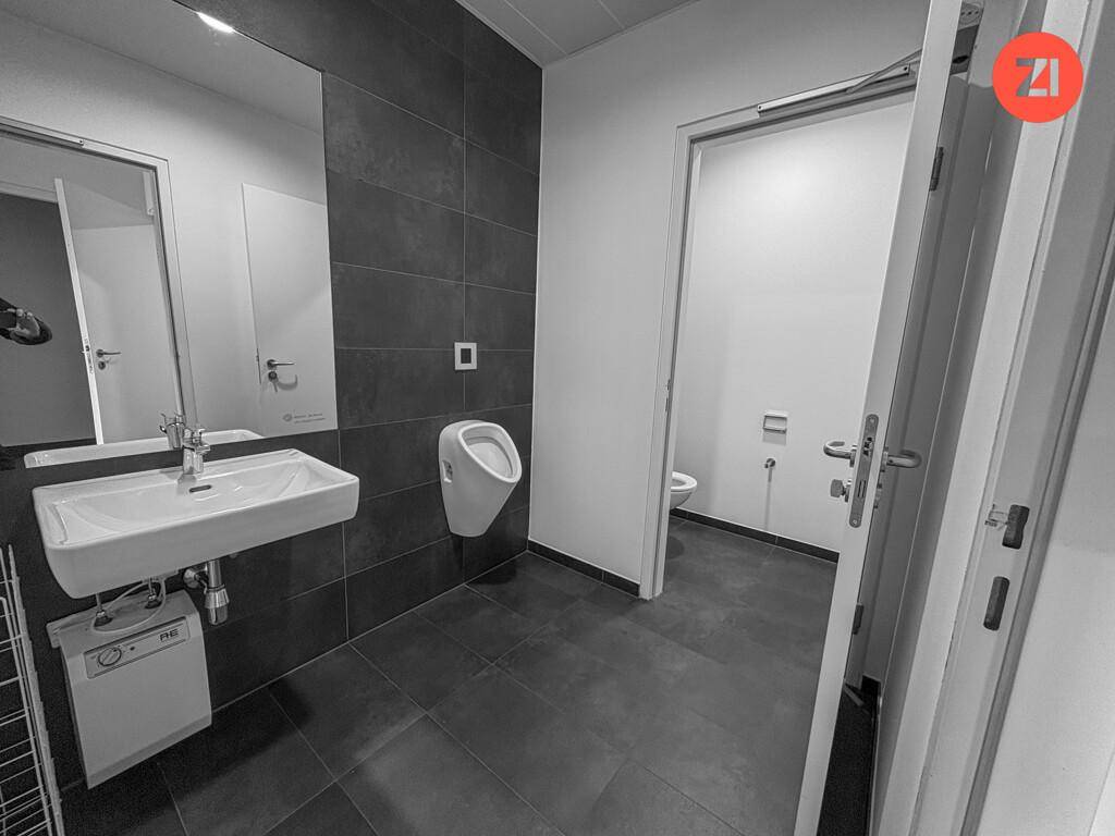 Modernes Badezimmer mit Urinal, Waschbecken und großem Spiegel, in Schwarz-Weiß-Tönen gehalten.