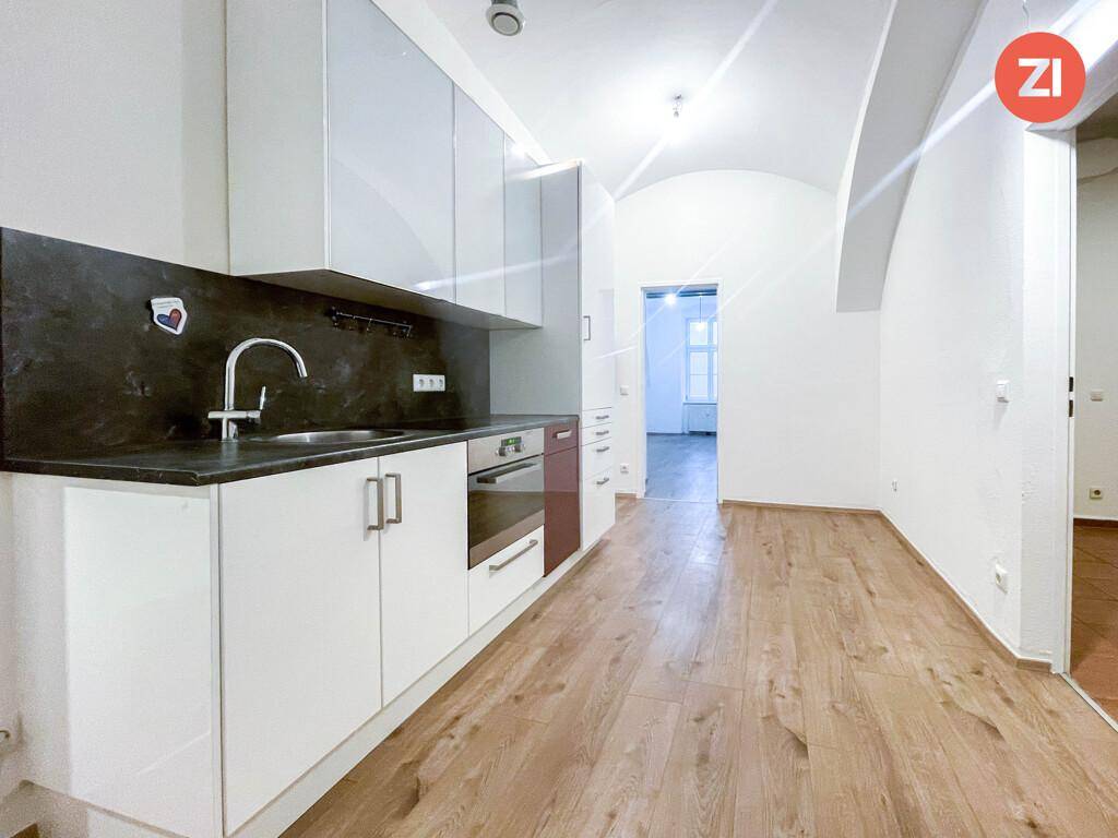 Moderne Küche mit weißen Schränken, dunkler Arbeitsplatte und Spüle, in einem Raum mit Holzboden.