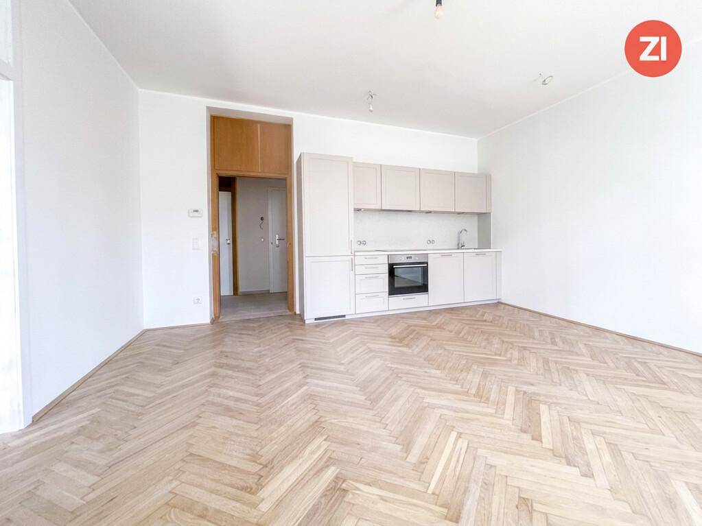 Heller Wohnraum mit Fischgrätparkettboden und integrierter, moderner Küchenzeile in neutralen Farben.