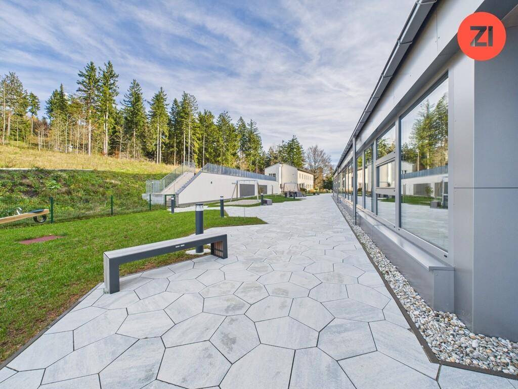 Moderner Außenbereich mit hexagonalen Pflastersteinen, umgeben von Rasenflächen und hohen Bäumen.
