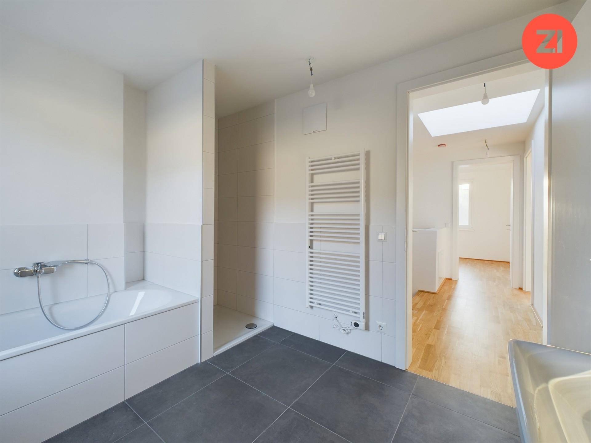 Badezimmer mit Badewanne, Duschbereich und beheiztem Handtuchhalter, alles in hellen Tönen gehalten.