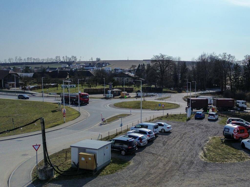 Blick auf einen Kreisverkehr und die ländliche Umgebung mit Feldern und Häusern unter klarem Himmel.