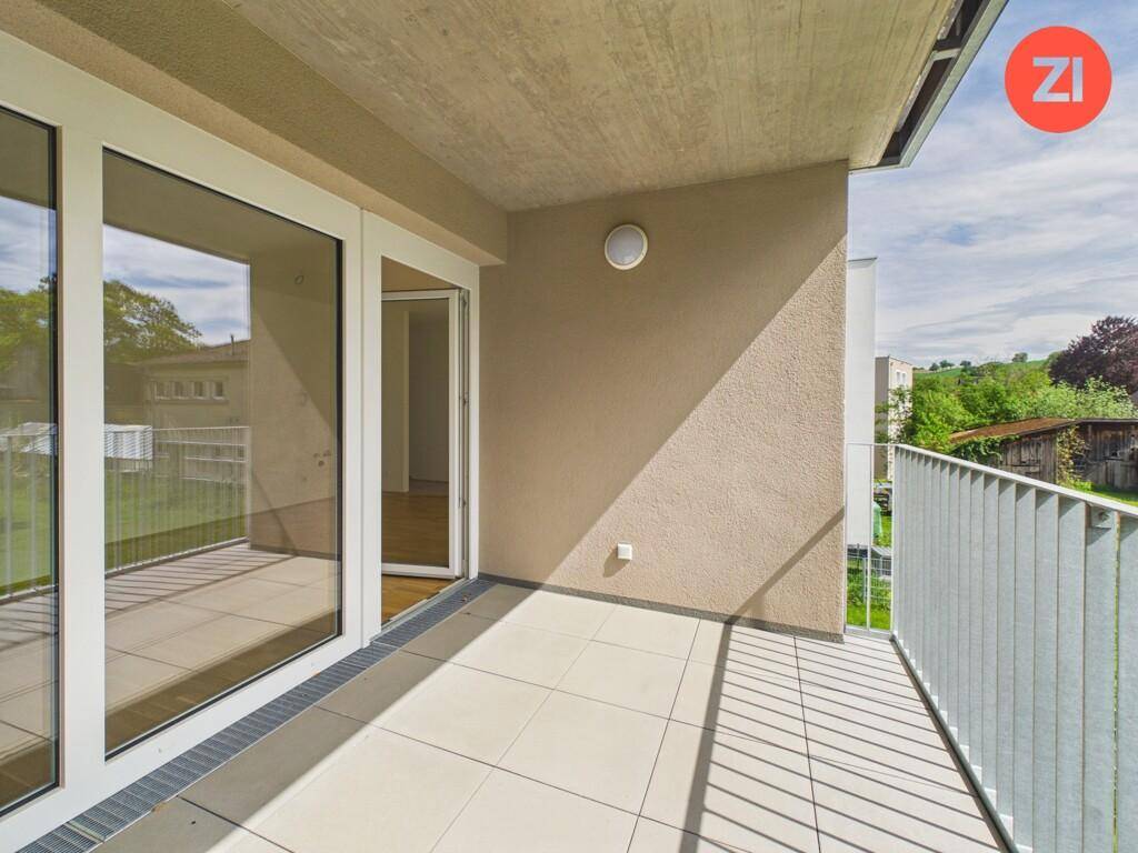 Geräumiger Balkon mit Fliesenboden und Metallgeländer, der einen angenehmen Blick ins Grüne bietet.