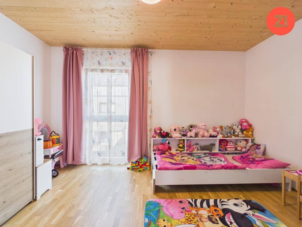 Kinderzimmer mit Holzboden, rosa Vorhängen und vielen Stofftieren, ideal für kleine Bewohner.