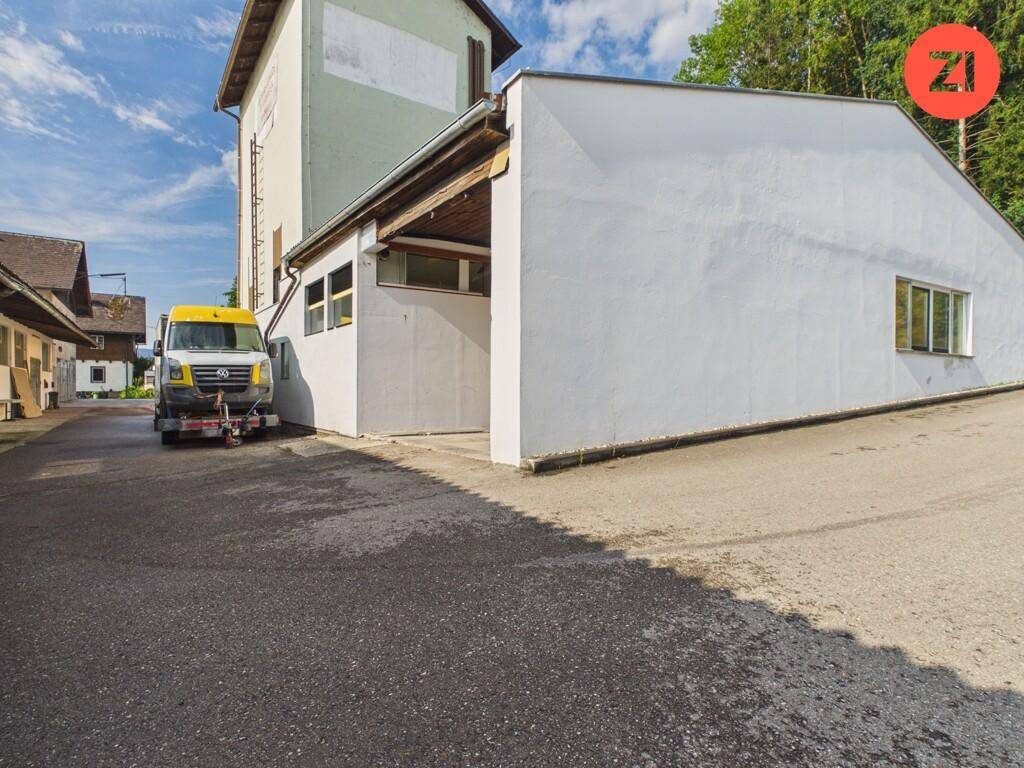 Gebäude mit weißer Fassade und Fenstern entlang einer asphaltierten Straße, umgeben von Bäumen.