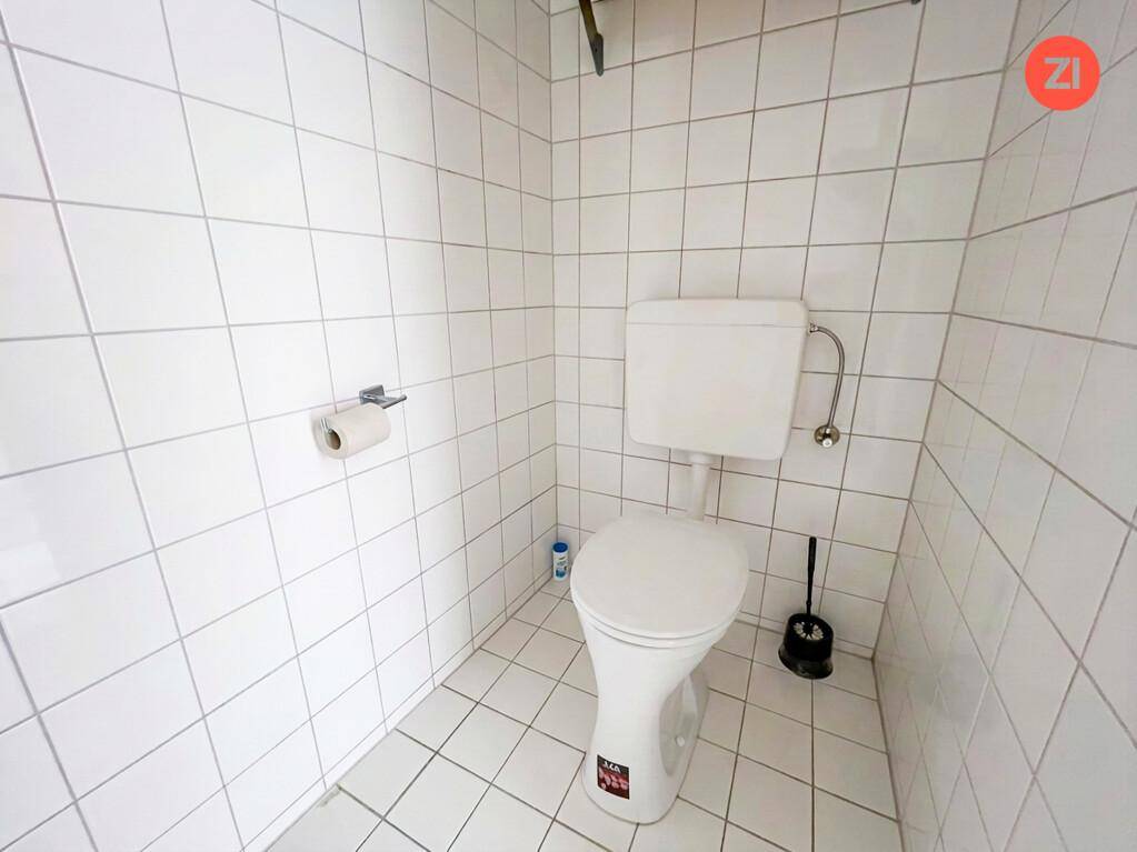 Kleines WC mit weißen Fliesen und einer Standardtoilette, sauber und funktional.