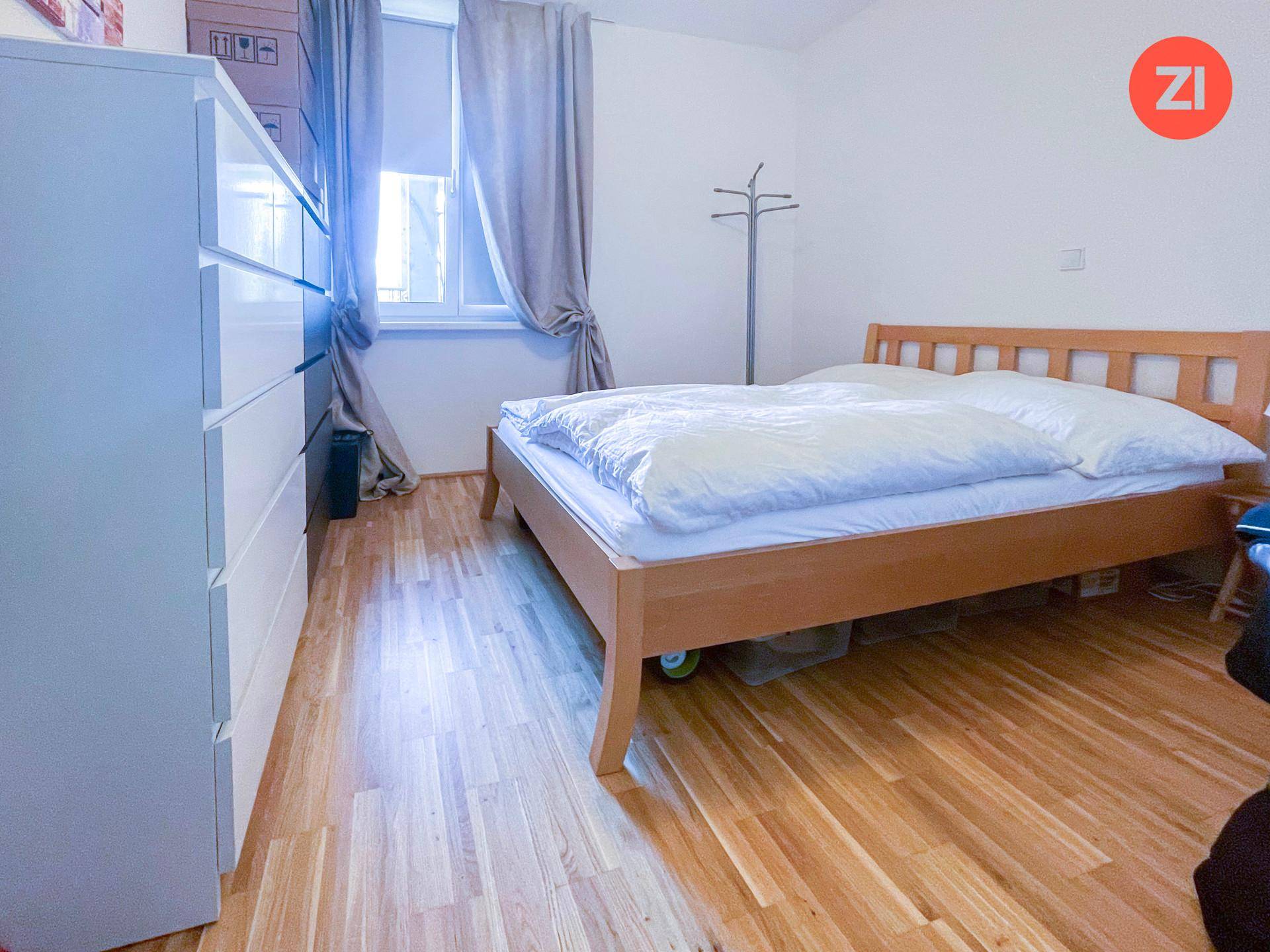 Gemütliches Schlafzimmer mit Holzbett, weißer Kommode und Fenster mit Vorhängen.