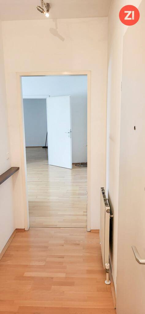Heller Eingangsbereich mit Holzfußboden, weiß gestrichenen Wänden und Blick in angrenzende Zimmer.