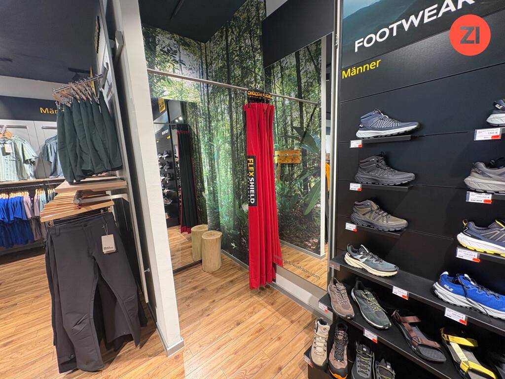 Umkleidebereich mit großem Spiegel und Waldmotiv-Tapete, daneben eine Präsentation von Sportschuhen.