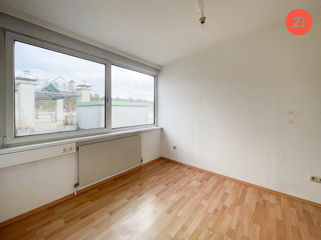 Leeres Zimmer mit Holzfußboden und großem Fenster, das einen Blick nach draußen bietet.