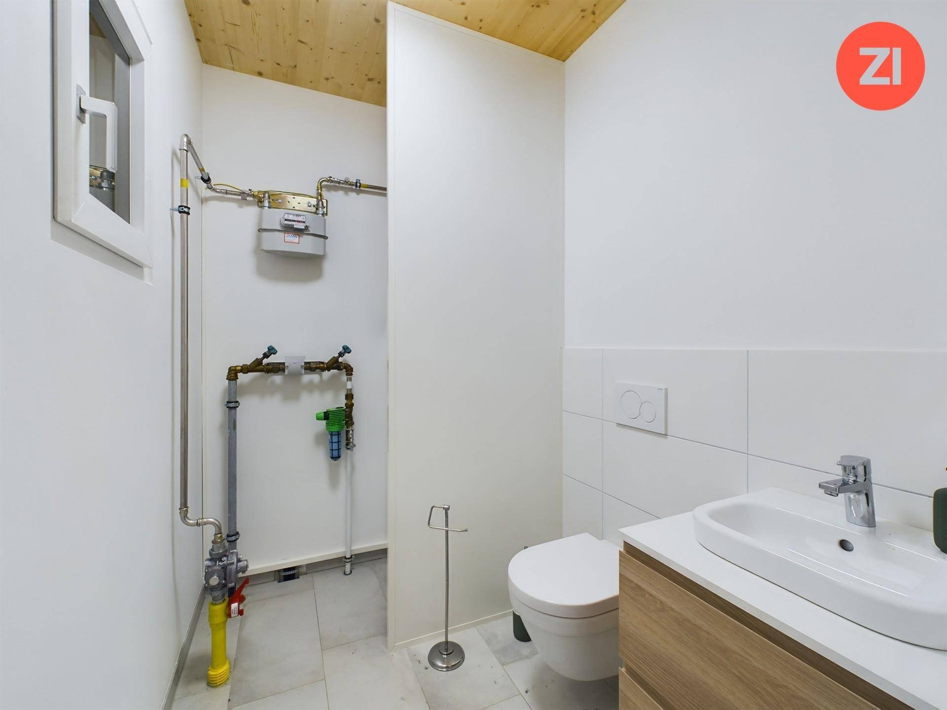 Gäste-WC mit WC, Waschbecken und sichtbaren Installationen unter einer Holzdecke.