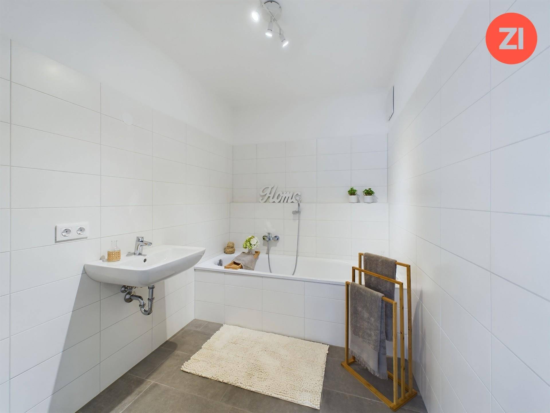 Modernes Badezimmer mit Badewanne, weißen Fliesen und Einzelwaschbecken.