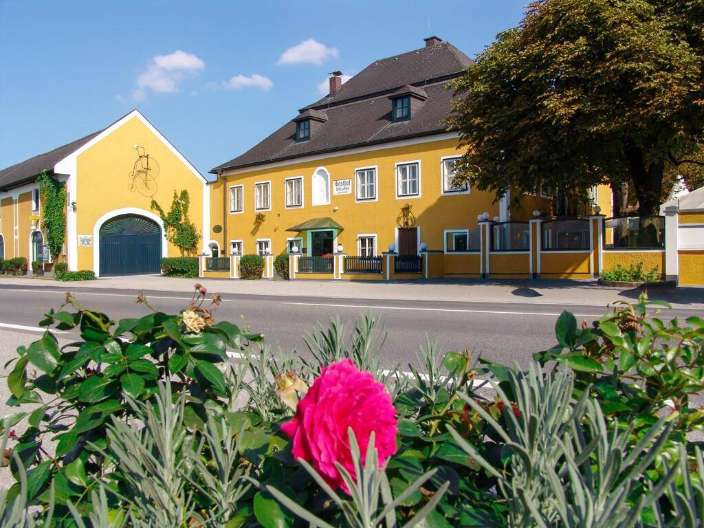 Gelbes historisches Gebäude mit Mansarddach und gepflegter Außenanlage an einer Straße.