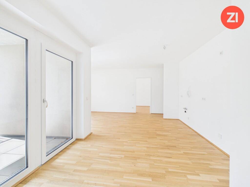 Helles, leeres Wohnzimmer mit Parkettboden und großen Fenstern, die viel Tageslicht hereinlassen.