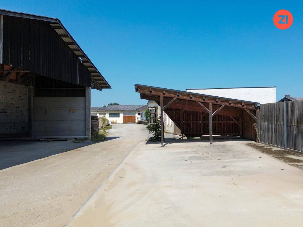 Unbefestigte Zufahrt zu einem Holzcarport und weiteren Gebäuden auf dem weitläufigen Grundstück.