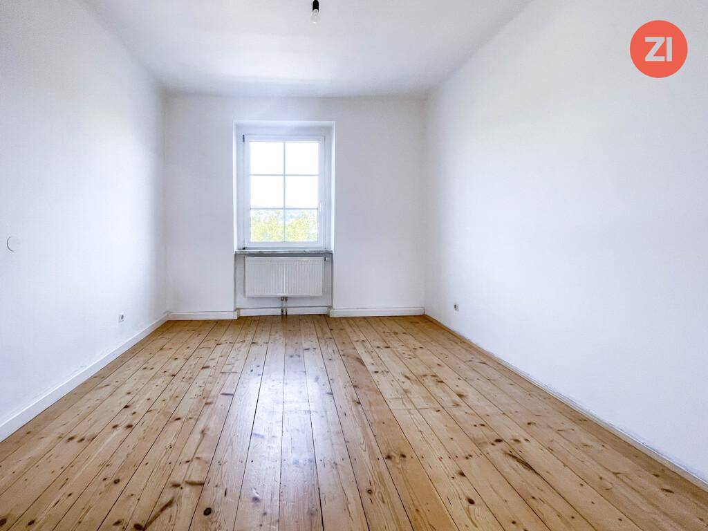 Helles Zimmer mit breiten Holzplanken und einem Fenster, ideal als Schlaf- oder Arbeitszimmer.