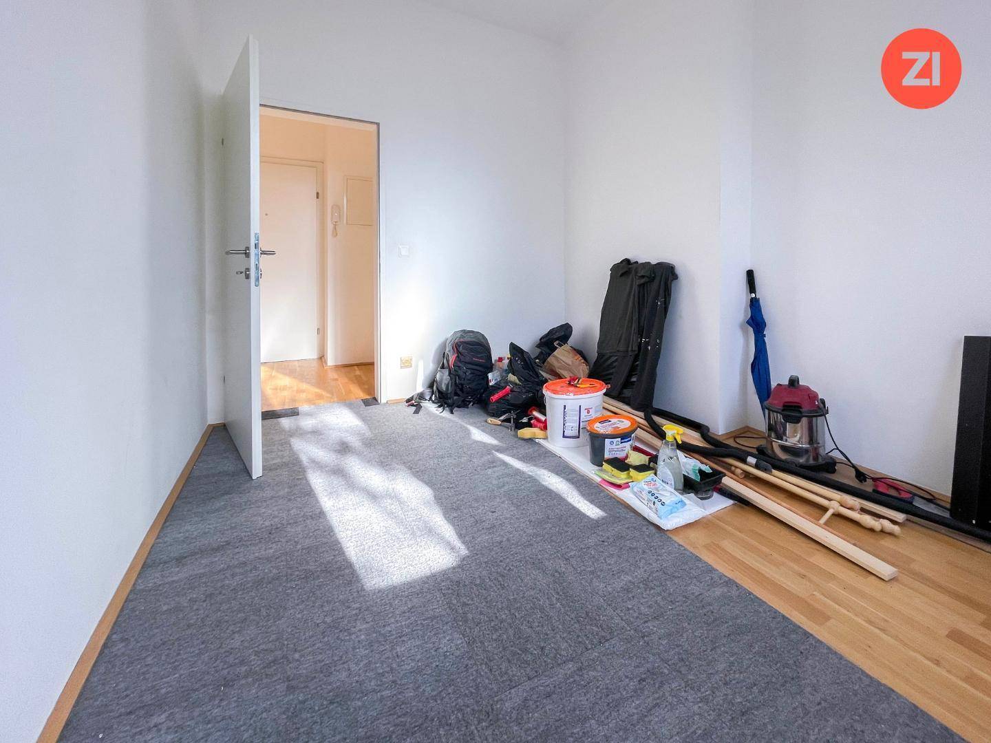 Renovierungsbedürftiges Zimmer mit Teppichboden und Holzboden, Blick in den Flur.