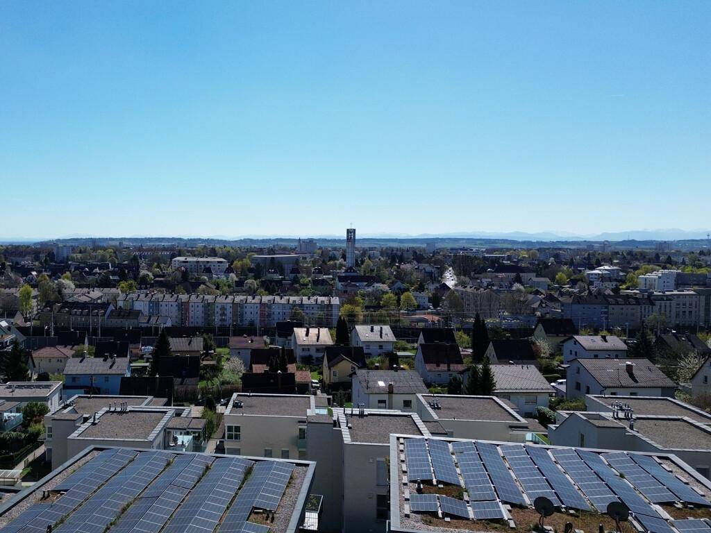 Weitläufiger Blick über die Stadt mit zahlreichen Dächern und Photovoltaikanlagen unter blauem Himmel.