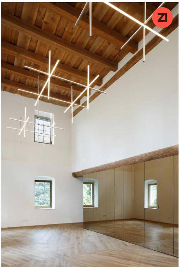 Geräumiger Mehrzweckraum mit hohen Decken, Holzbalken und einer verspiegelten Wand, beleuchtet durch moderne Leuchten.