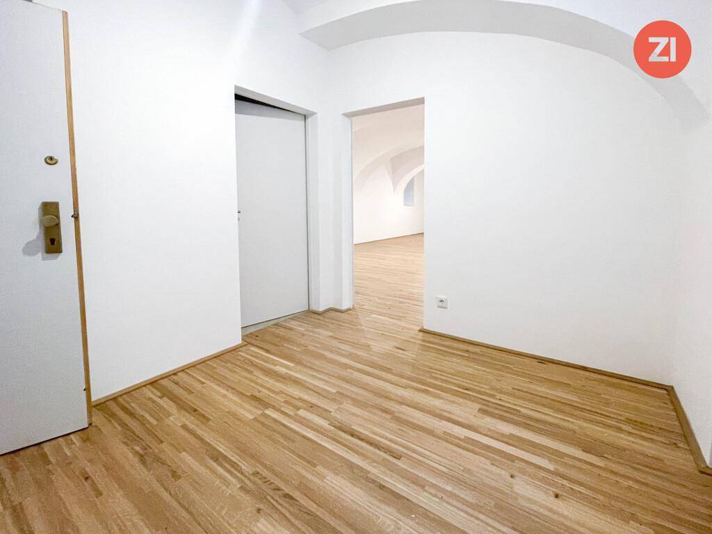 Heller Flur mit Holzboden und weiß gestrichenen Wänden, der zu weiteren Räumen führt.