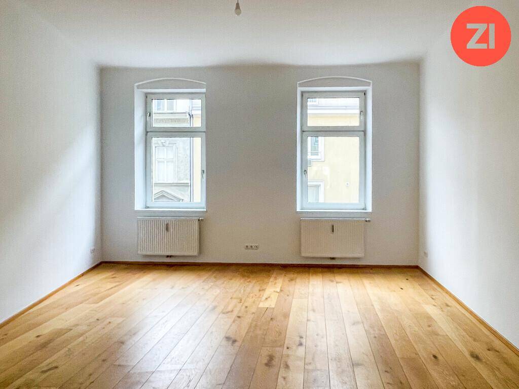 Heller Raum mit neu verlegtem Holzparkettboden und zwei großen Fenstern.